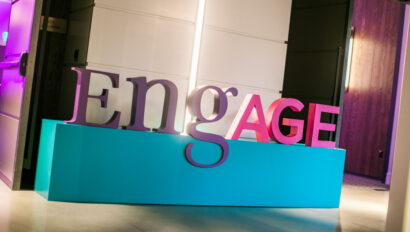 Large "engage" sign in pink and white letters displayed indoors at an event venue space.