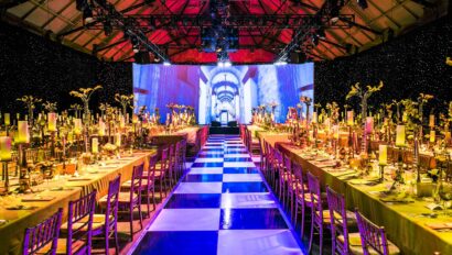 Grand banquet hall set for a formal event by an event planning company, with a blue and white checkerboard aisle, decorated tables, and a large projected image on the wall.