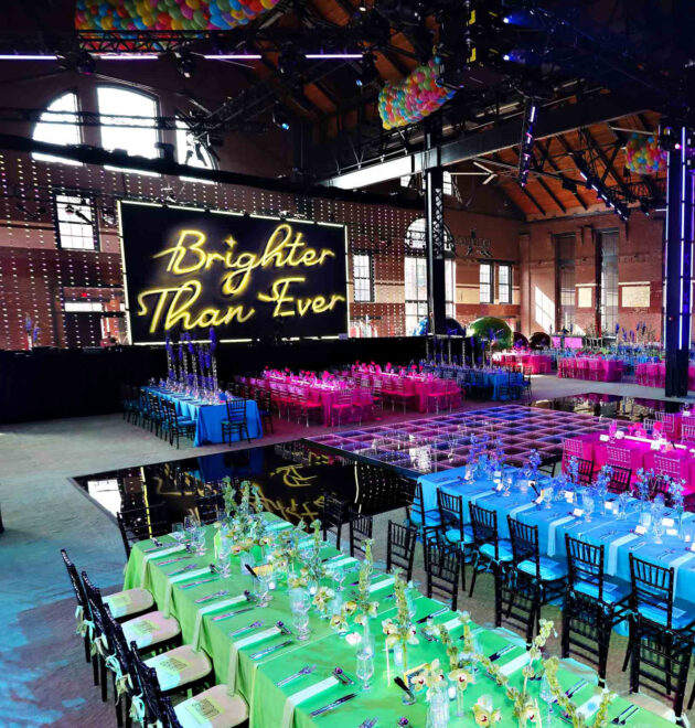 An event venue space set up for a function with vibrant lighting and a "brighter than ever" sign on the stage.