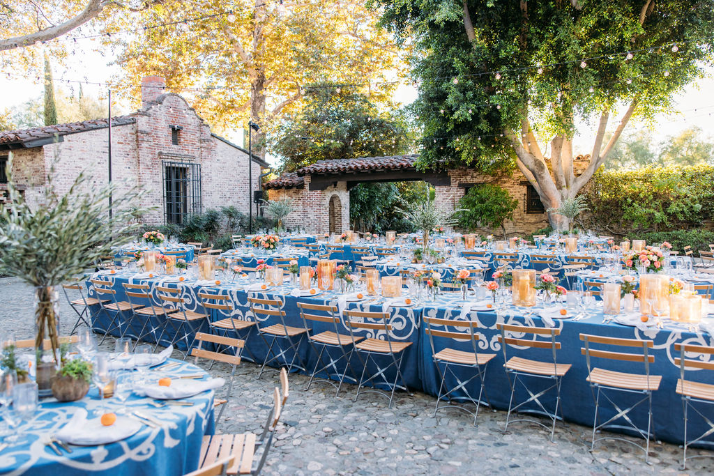 Outdoor courtyard dinner setting under a canopy of trees and twinkling lights.